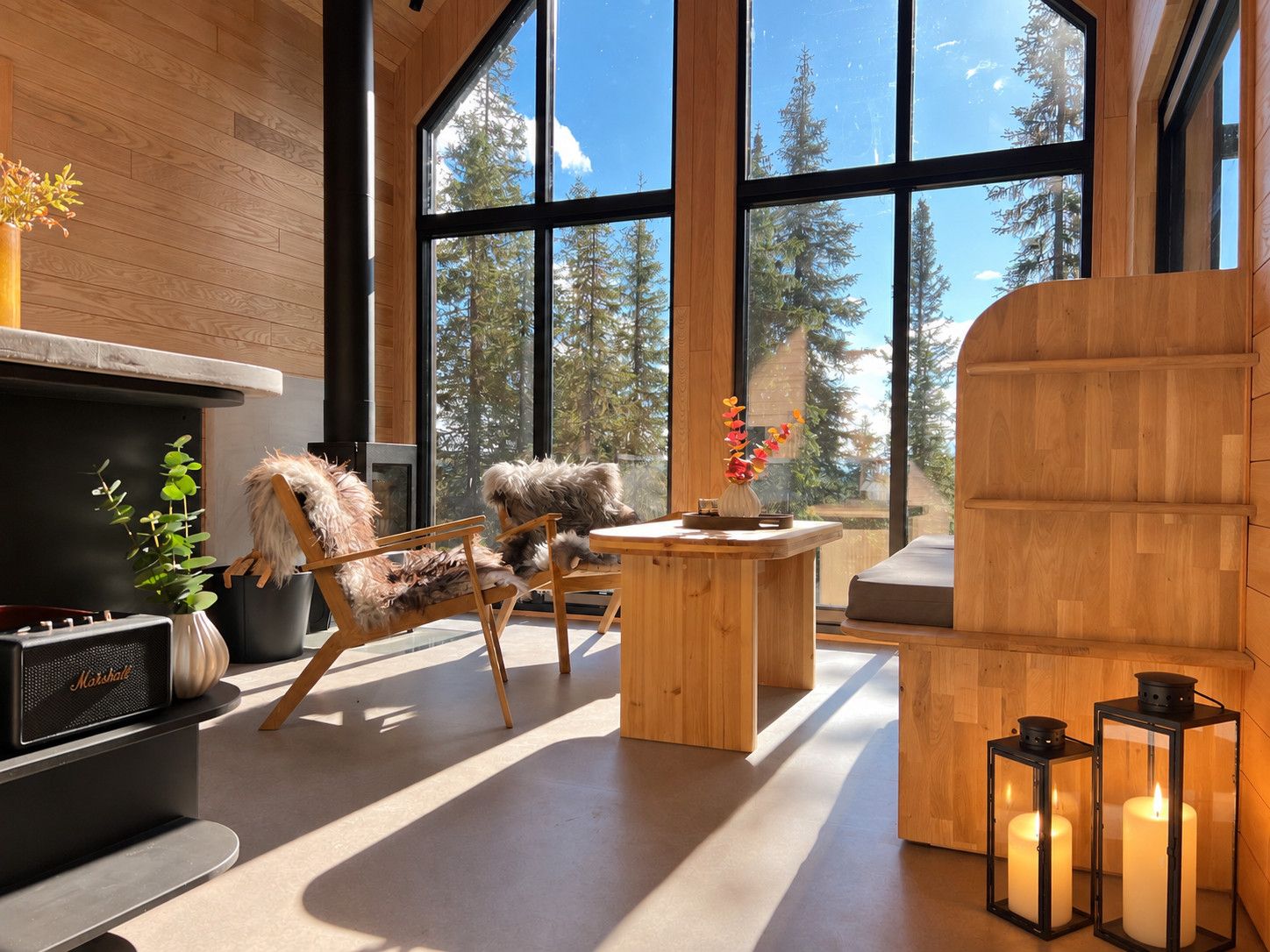 Un interior moderno con chimenea, muebles de madera y ventanas amplias que ofrecen vista a árboles.