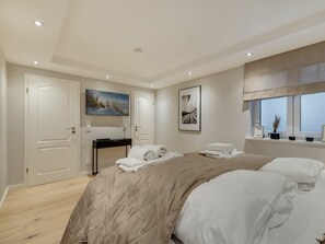 A modern bedroom with a large bed, a bedside table, a mirror, and artwork on the walls. - Lighthouse - New, Exclusive, Close to the Beach (Sylt)