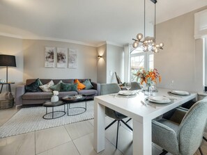 A modern living room with a sofa, coffee table, and dining table set for a meal. - Lighthouse - New, Exclusive, Close to the Beach (Sylt)