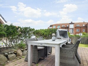 An outdoor patio with a table and wicker chairs, a grill, and a stone wall. - Lighthouse - New, Exclusive, Close to the Beach (Sylt)