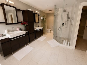 Un baño moderno con un espejo grande, dos lavamanos, ducha y un inodoro.