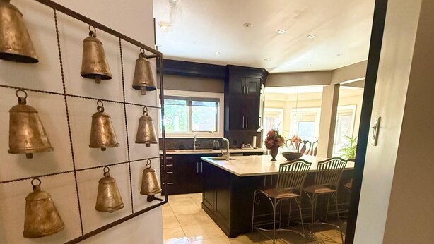 Une cuisine moderne dotée d’un îlot central, de meubles de rangement aux couleurs sombres et d’une collection de cloches décoratives fixée au mur.