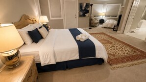 Une chambre à coucher comprenant un lit, des tables de chevet, une lampe, un tapis et une porte donnant sur une autre pièce.