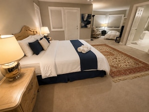 Un dormitorio con una cama, mesitas de noche, una lámpara, un tapete y una puerta que da a otra habitación.