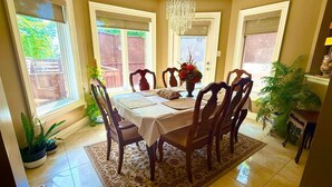 Un coin repas avec une table dressée pour six personnes, entourée de chaises, d’un lustre et de plantes en pot.