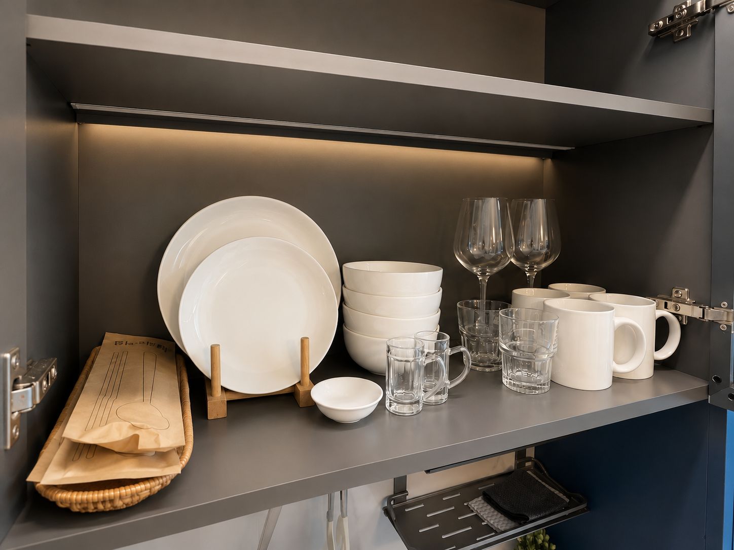 A kitchen shelf with white plates, bowls, glasses, and mugs.