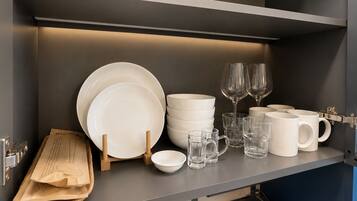 A kitchen shelf with white plates, bowls, glasses, and mugs.