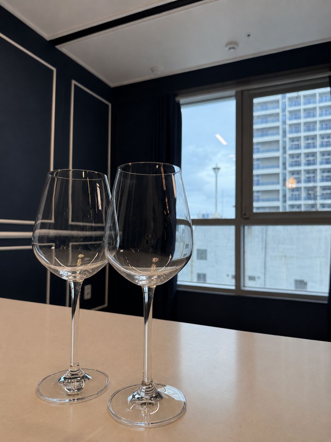 Two empty wine glasses on a table in a room with a view of a cityscape through a large window.