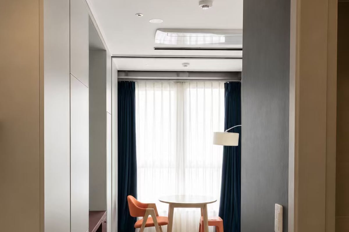 A hotel room with a bed, a desk, and a chair. There is a window with curtains and a ceiling light.