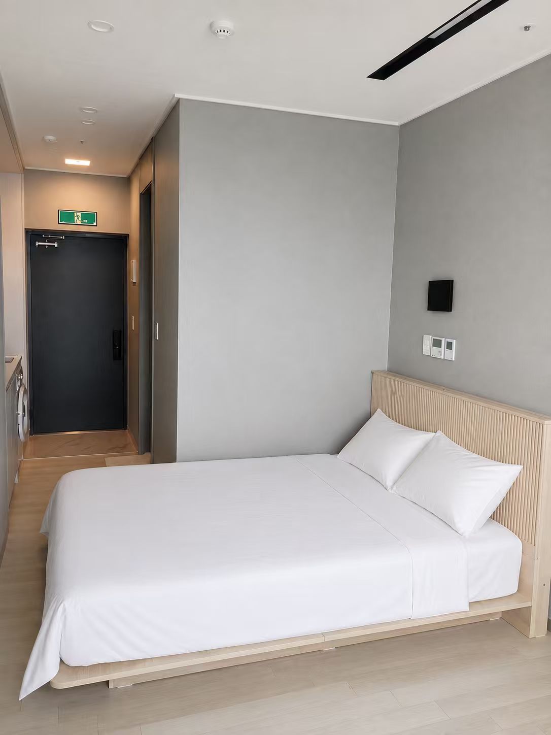 Una habitación de hotel moderna con una cama grande, cabecera de madera y pared gris.