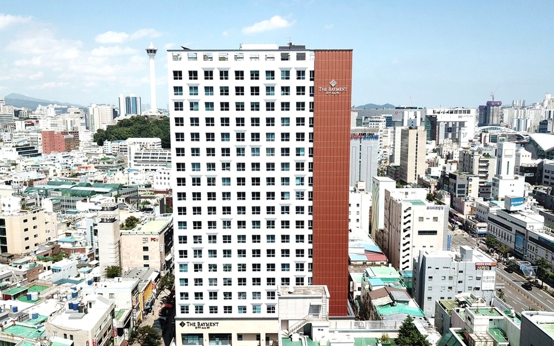 A high-rise hotel with a prominent red and white facade, multiple floors, and a view of the surrounding cityscape.