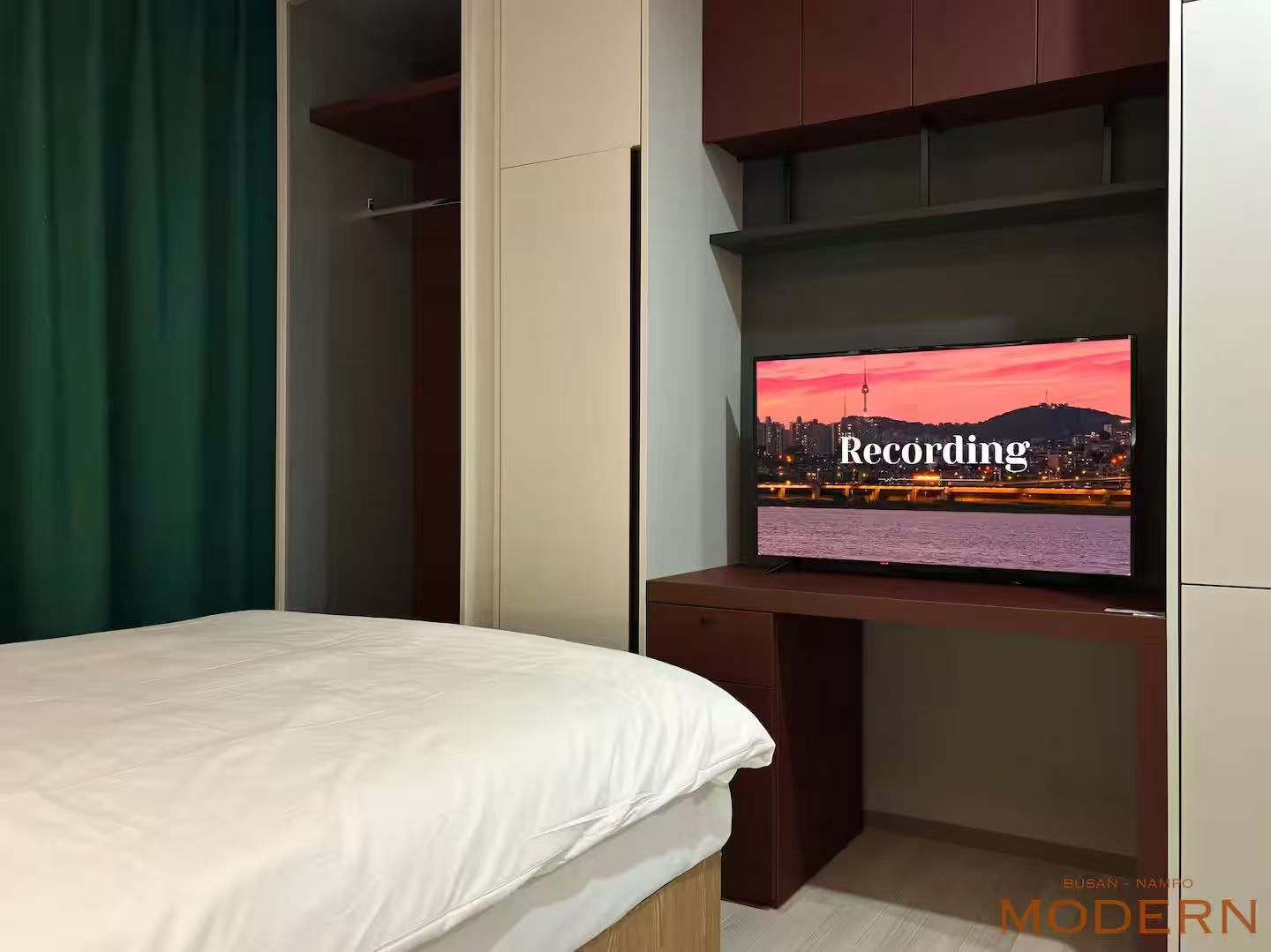 A hotel room with a bed, a television displaying a cityscape, and a wardrobe.