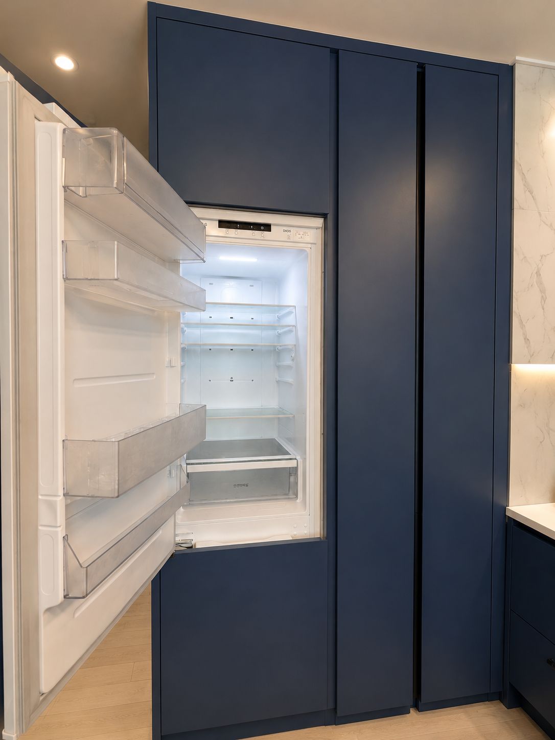 Una cocina moderna con refrigerador empotrado, encimera de mármol y un mueble de color azul oscuro.