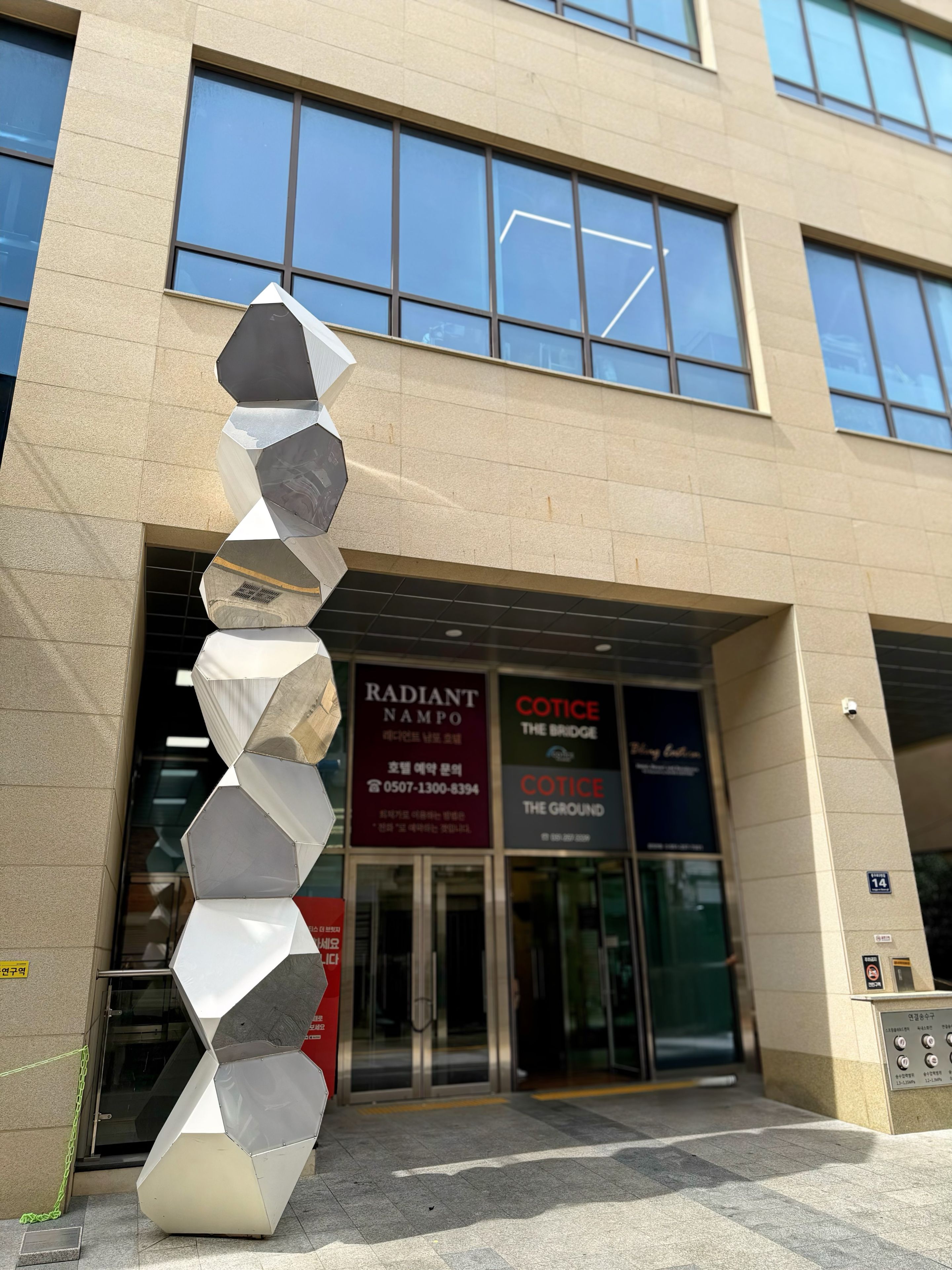 A modern building facade with large windows and a unique geometric sculpture in front.