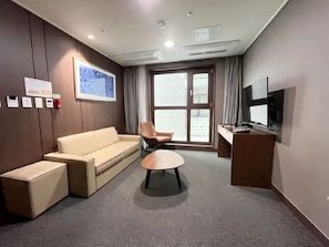 A hotel room with a sofa, armchair, small table, TV, and a window with curtains. - STAY NAMPO PREMIER (Busan)