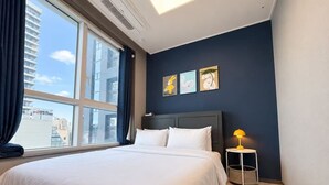 Habitación de hotel con una cama grande, una mesita de noche con lámpara y vistas a la ciudad a través de un ventanal.
