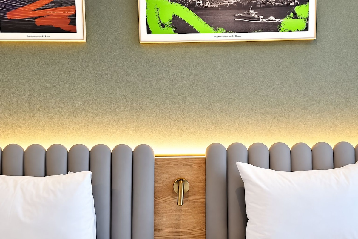 A hotel room with a modern headboard, two white pillows, and two framed artworks above the bed.