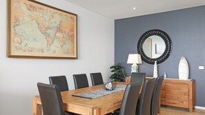 A dining area with a wooden table, black chairs, a world map on the wall, a round mirror, and a plant. - Paradise Penthouse Ocean Views (The Entrance North)