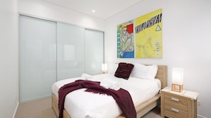 A bedroom with a bed, bedside tables, a wardrobe, and a large abstract painting on the wall. - Paradise Penthouse Ocean Views (The Entrance North)