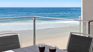Een balkon met uitzicht op de oceaan, twee stoelen en twee glazen met een donker drankje.