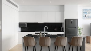 A modern kitchen with a central island, black appliances, and a minimalist design. - Paradise Penthouse Ocean Views (The Entrance North)