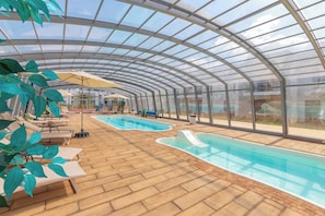 Ein Hallenbad mit Glasdach, Liegestühlen und einer Rutsche.
