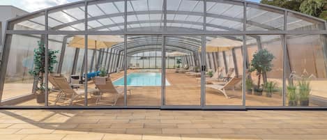 Un área de piscina exterior con paredes de cristal, sillas de descanso y plantas en macetas.