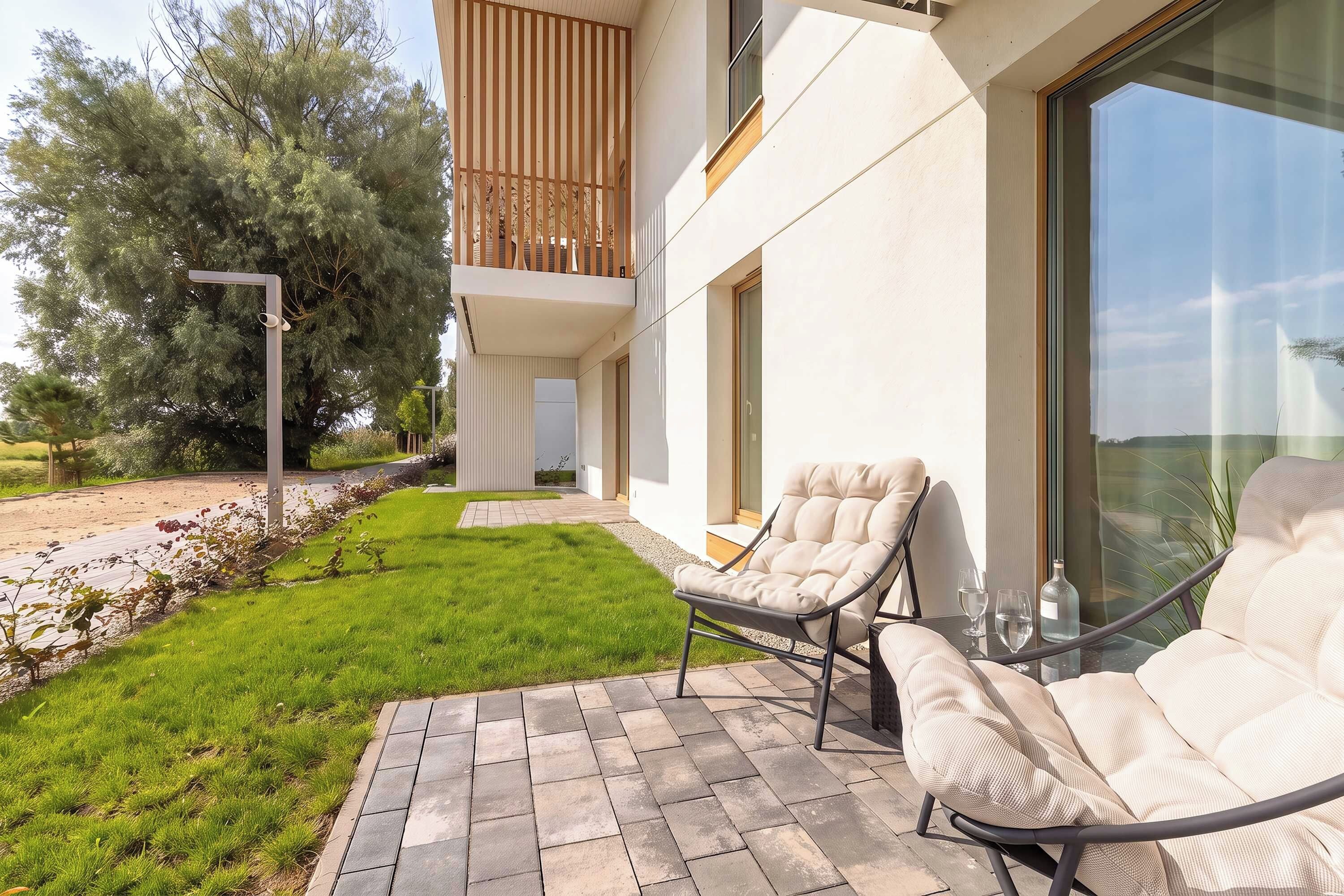 Un área de estar exterior moderna con dos sillones reclinables y una mesa de vidrio, un patio empedrado y vistas del paisaje circundante.