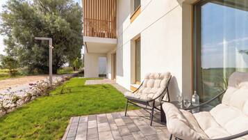 Un área de estar exterior moderna con dos sillones reclinables y una mesa de vidrio, un patio empedrado y vistas del paisaje circundante.