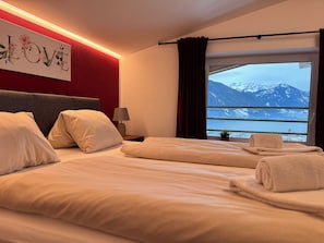 Hotelkamer met een bed, nachtkastje, lamp, raam met uitzicht op bergen en een muur met een 'LOVE' bord.