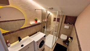 Et moderne badeværelse med glasvæg omkring brusenichen, en indbygget vaskemaskine og et toilet.