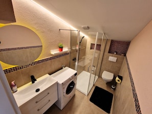 Een moderne badkamer met een douche met glazen wand, een inbouw wasmachine en een toilet.