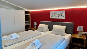 Et hotelværelse med to senge, en rød accentvæg, et kunstværk med teksten 'LOVE' og pænt foldede håndklæder.