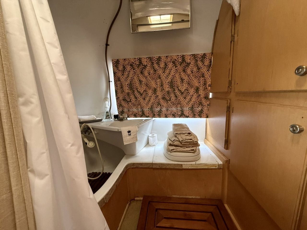 Casa de banho compacta com lavatório, pilha de toalhas e parede estampada.