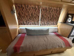 Een klein bed met hoofdeinde, een kussen en een deken met een rode streep.