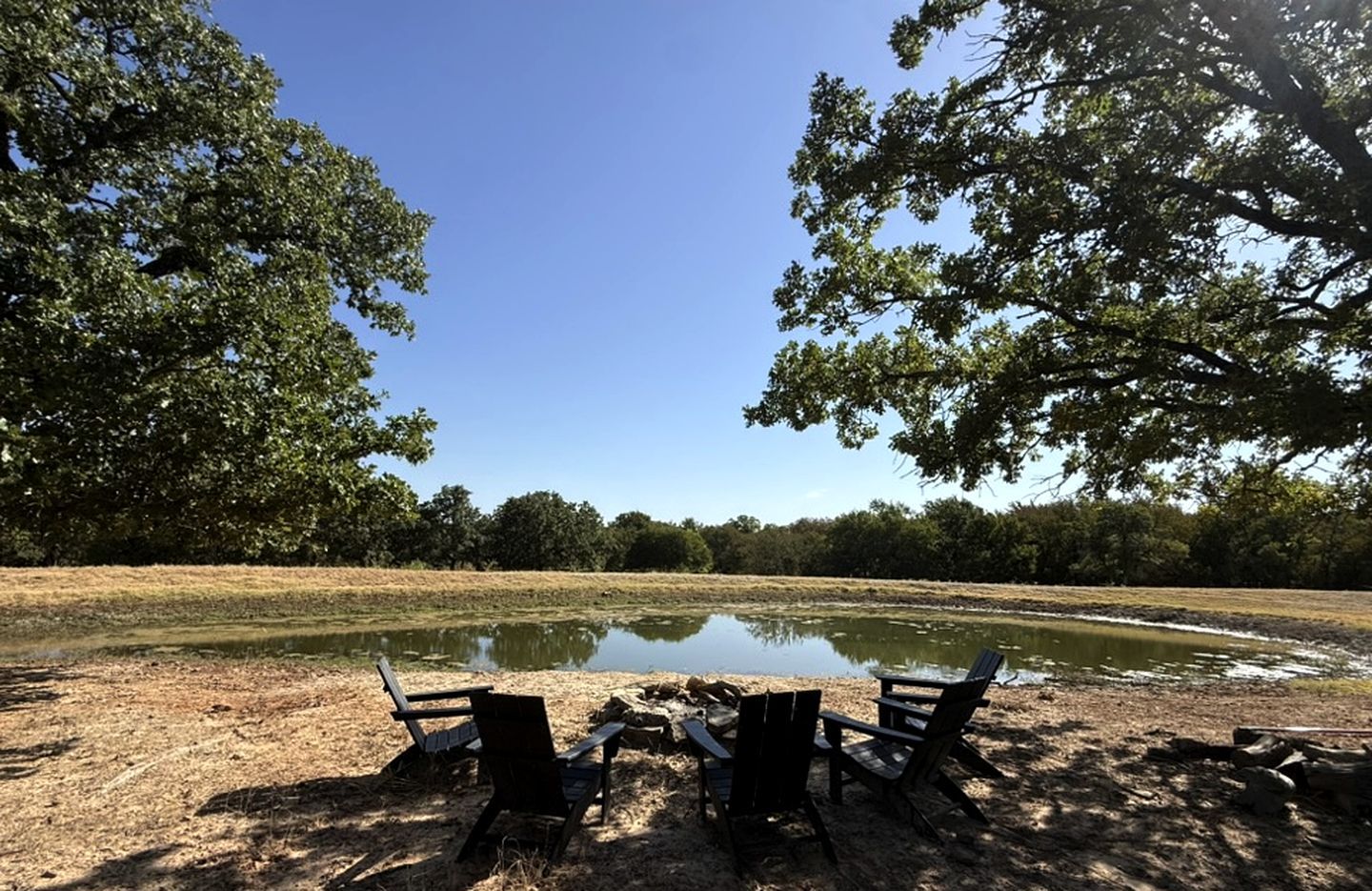 Een oeverlandschap met een picknicktafel en stoelen, omgeven door bomen en een rustig wateroppervlak.