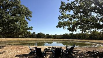 Een oeverlandschap met een picknicktafel en stoelen, omgeven door bomen en een rustig wateroppervlak.