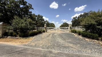 Une allée de gravier mène à une entrée fermée par un portail, avec un bâtiment en pierre situé sur la gauche.