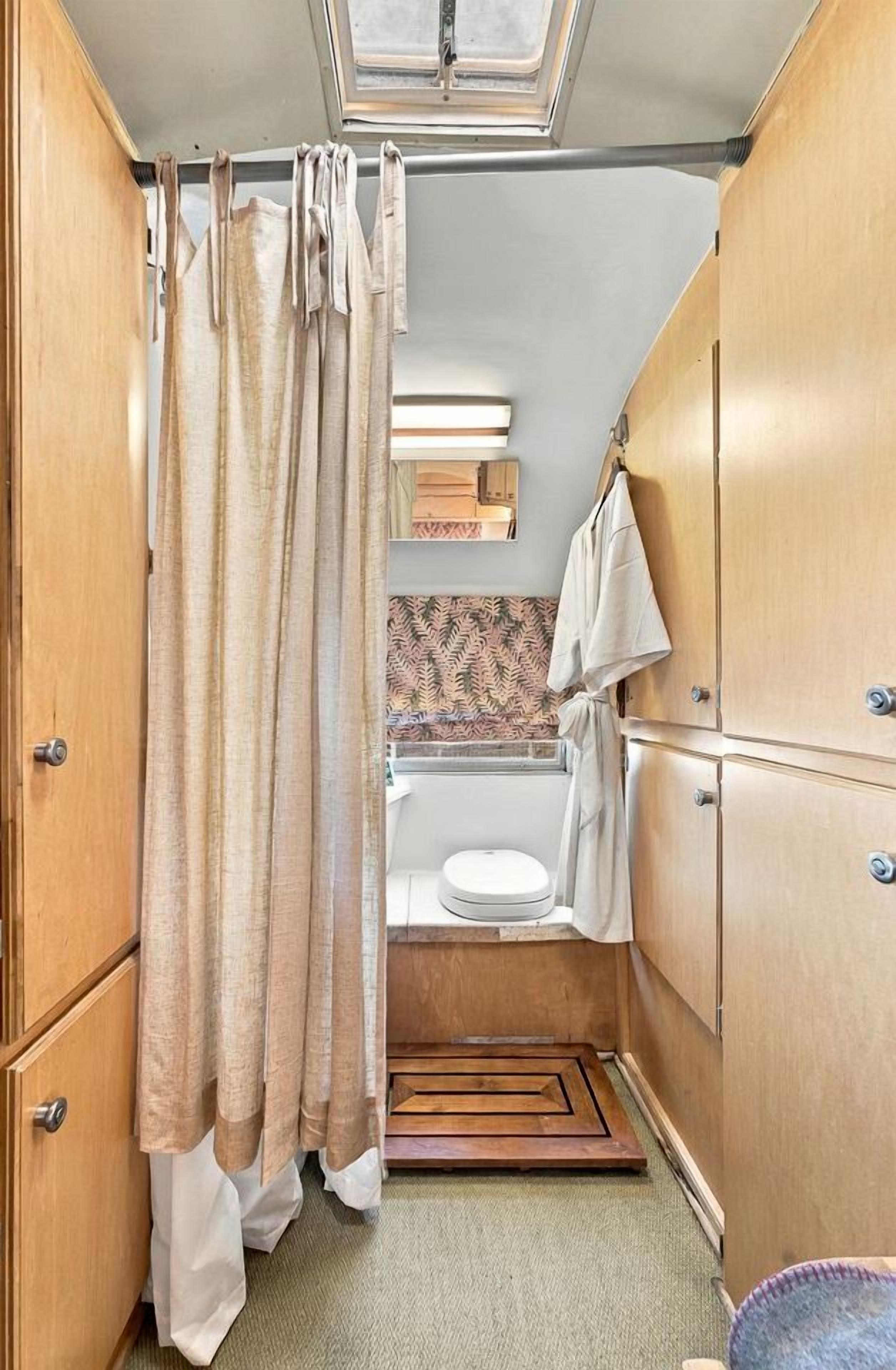 A compact RV bathroom with a shower curtain, a toilet, a sink, and wooden cabinets.
