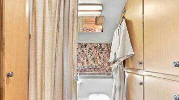 A compact RV bathroom with a shower curtain, a toilet, a sink, and wooden cabinets.