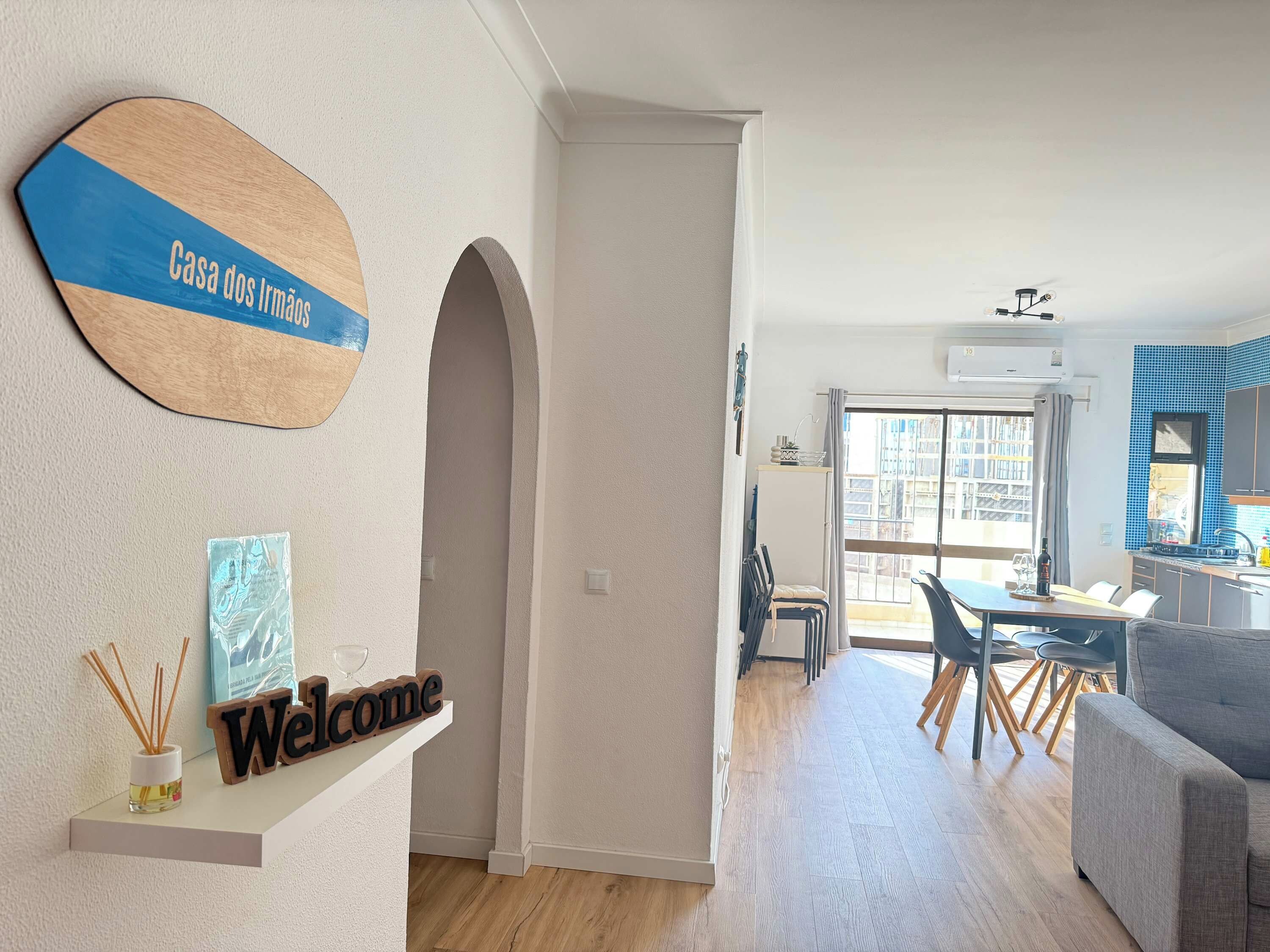 A modern interior with a 'Welcome' sign, a 'Casa dos Irmãos' sign, a dining area, and a kitchen.