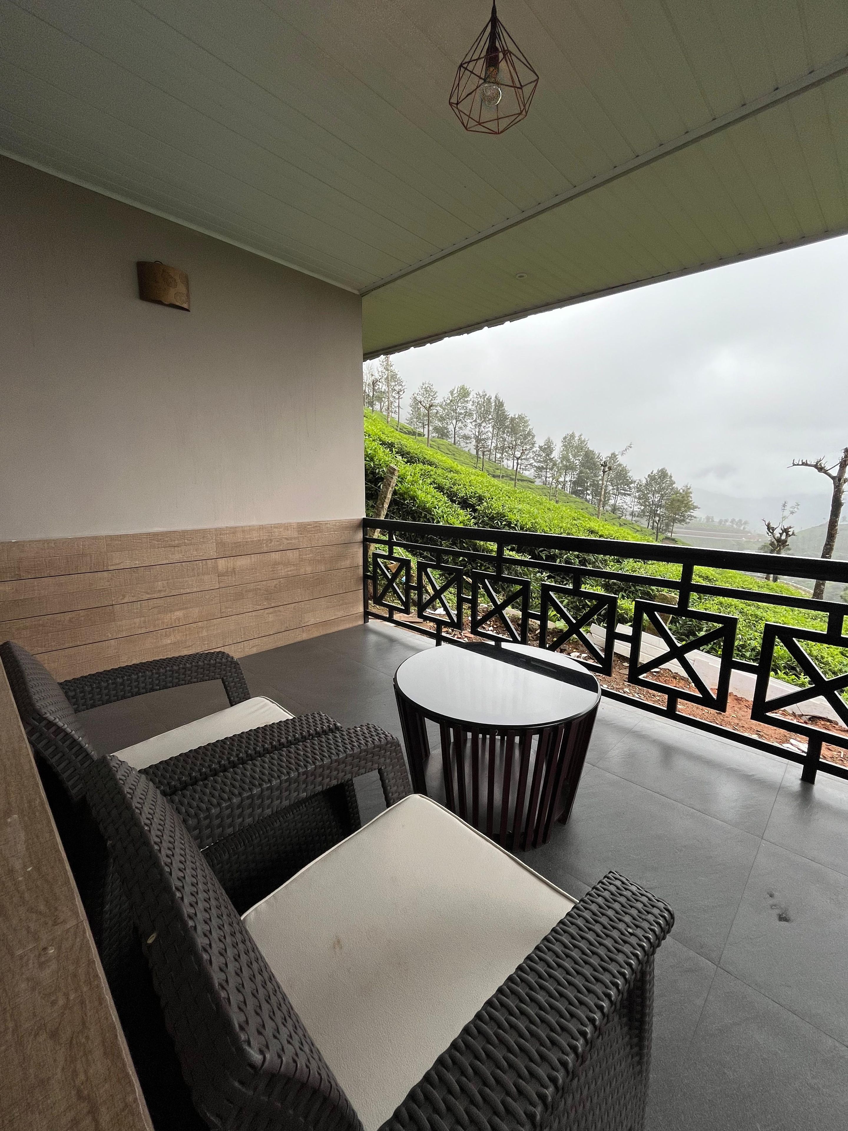 Un espacio de estar techado al aire libre con muebles de mimbre y una mesa, con vista a un paisaje montañoso.
