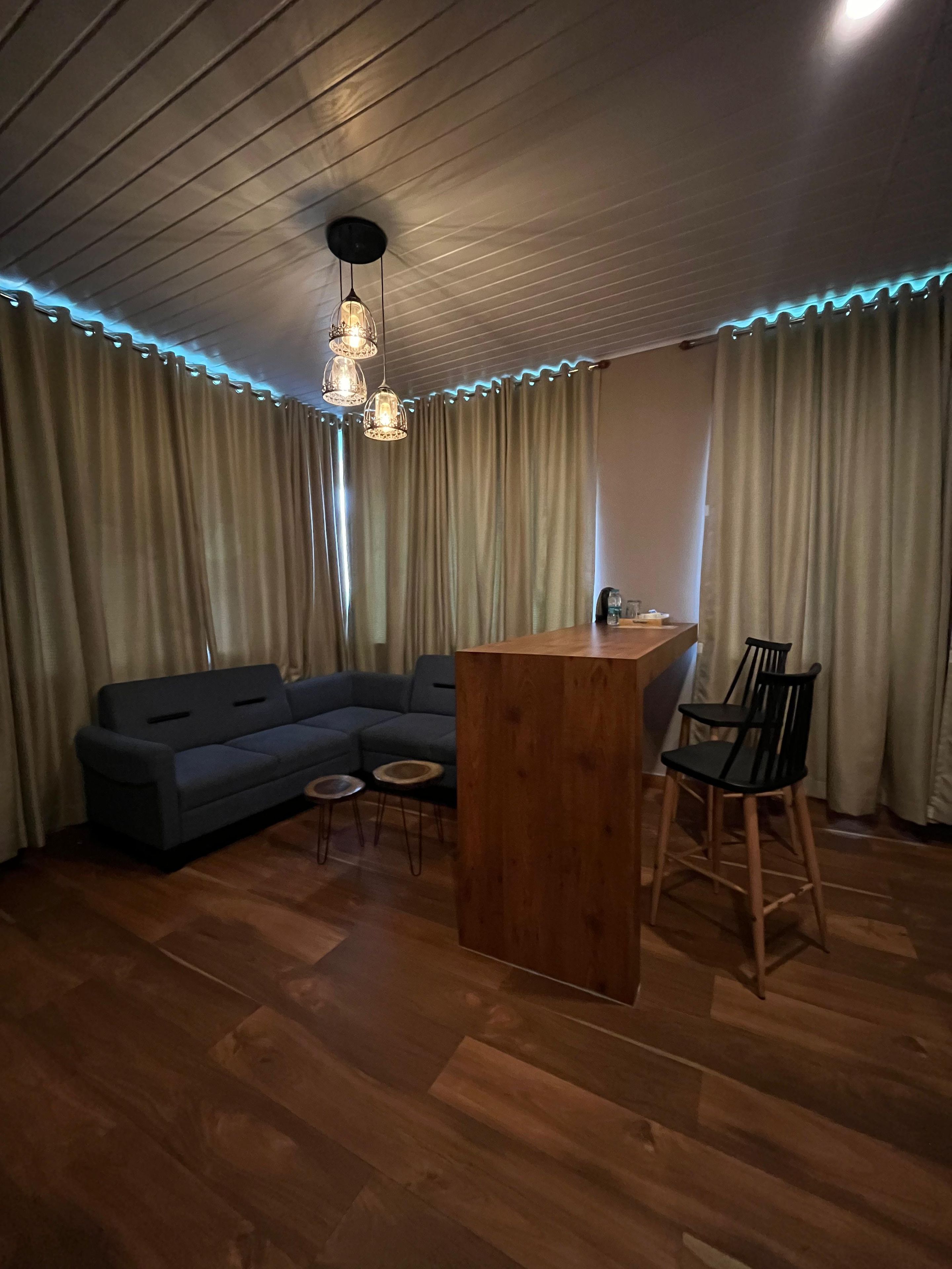 Una habitación con piso de madera, un sofá, una mesa redonda pequeña, una zona de bar y una silla.