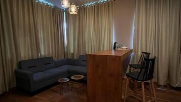 Una habitación con piso de madera, un sofá, una mesa redonda pequeña, una zona de bar y una silla.
