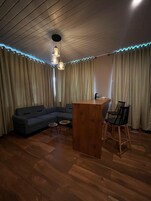 Una habitación con piso de madera, un sofá, una mesa redonda pequeña, una zona de bar y una silla.