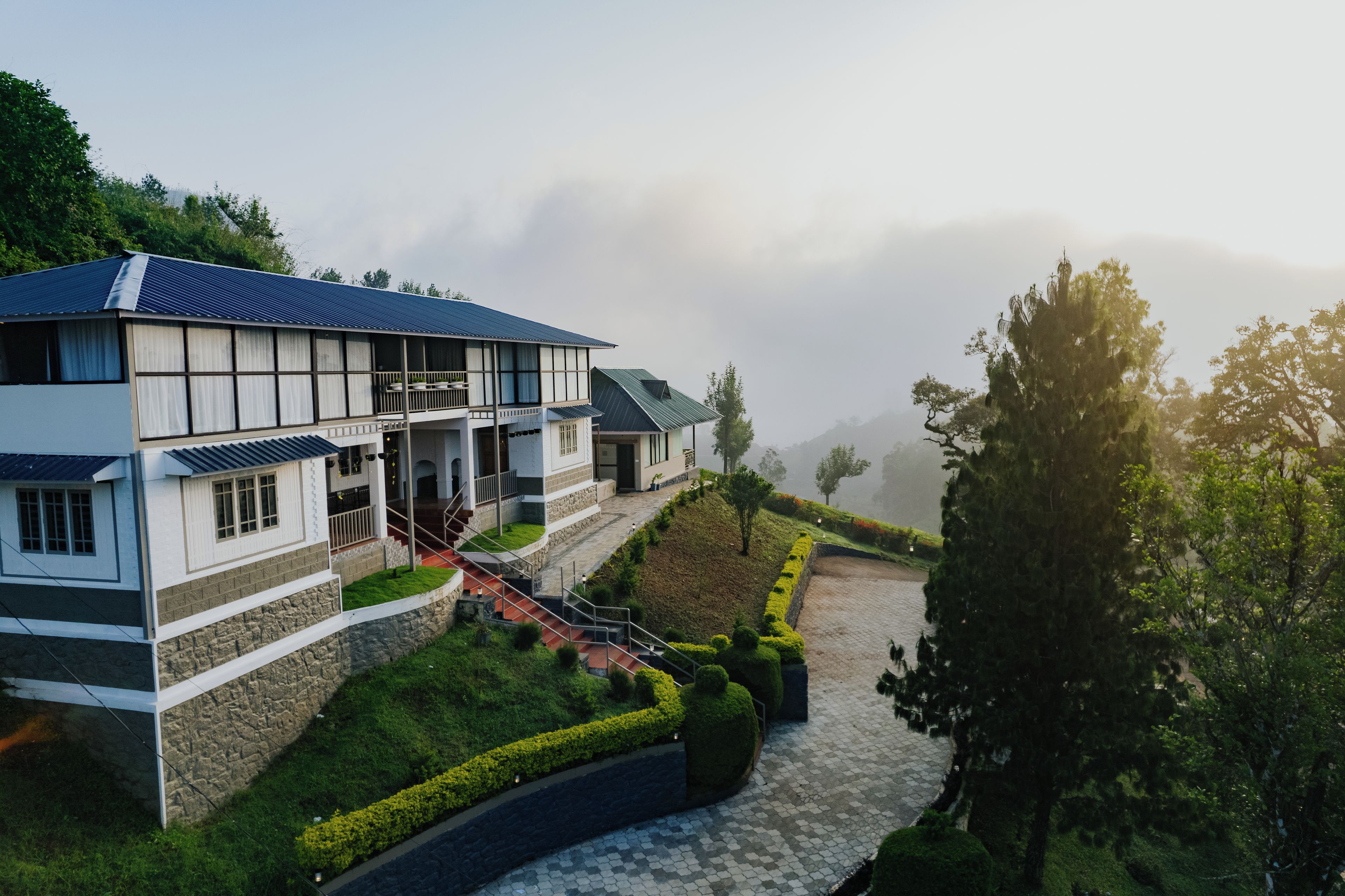 A two-story building with a balcony, a stone wall, and a paved pathway leading to the entrance.
