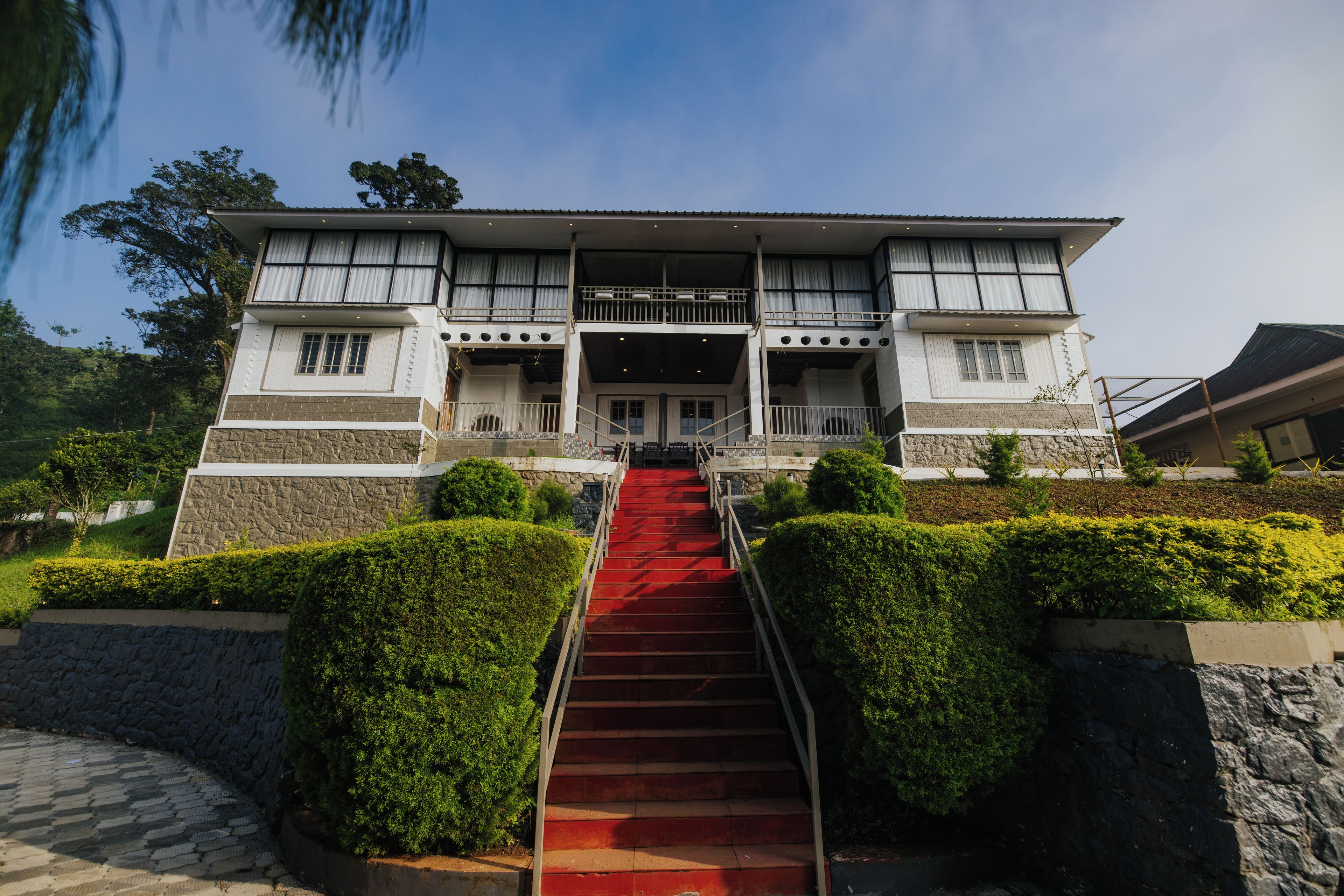 Un edificio de dos pisos con una escalera alfombrada de color rojo que lleva a un balcón con cortinas blancas.