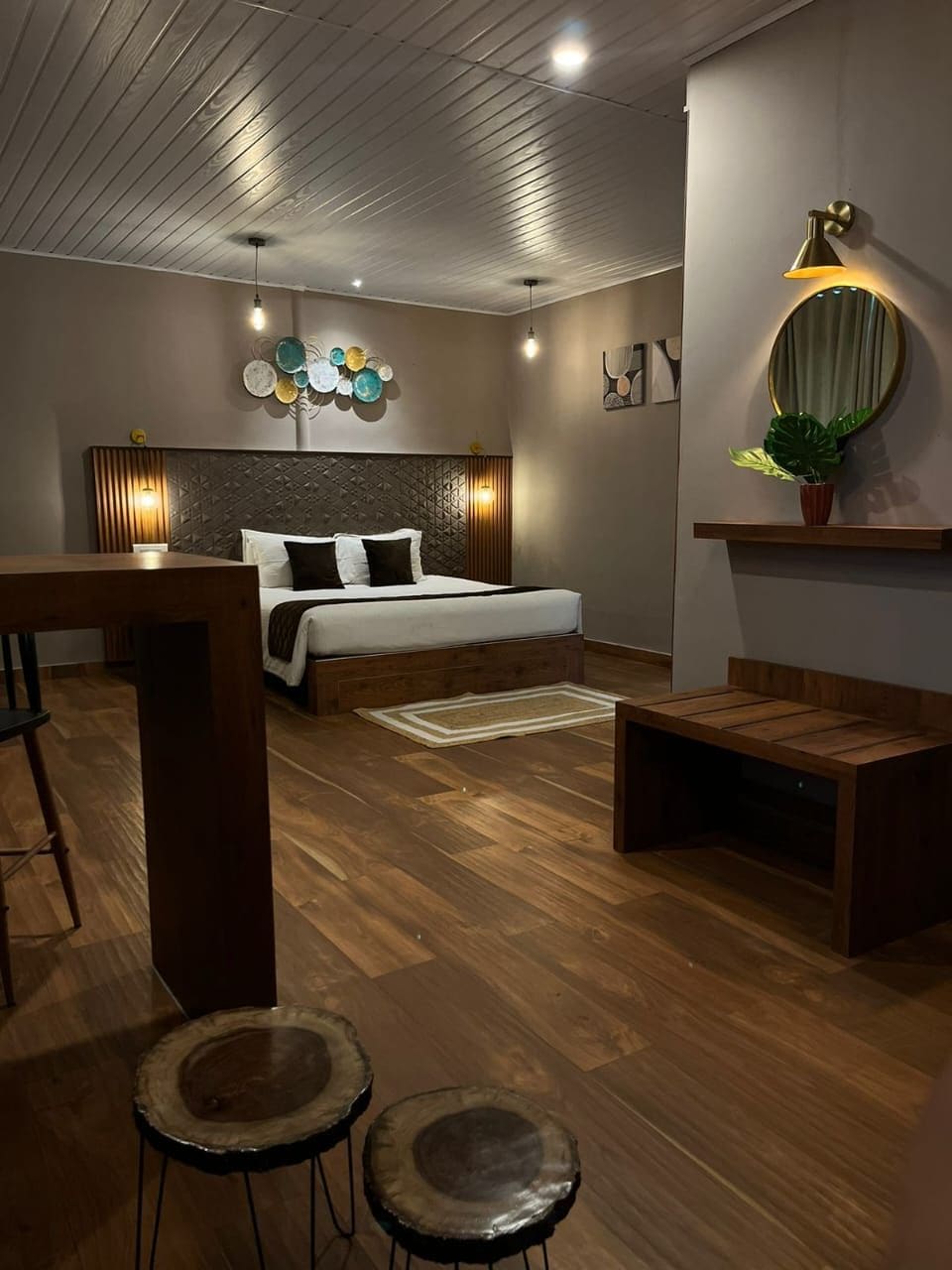 Un dormitorio moderno con piso de madera, una cama con ropa blanca, un cabecero con diseño geométrico y un espejo montado en la pared.