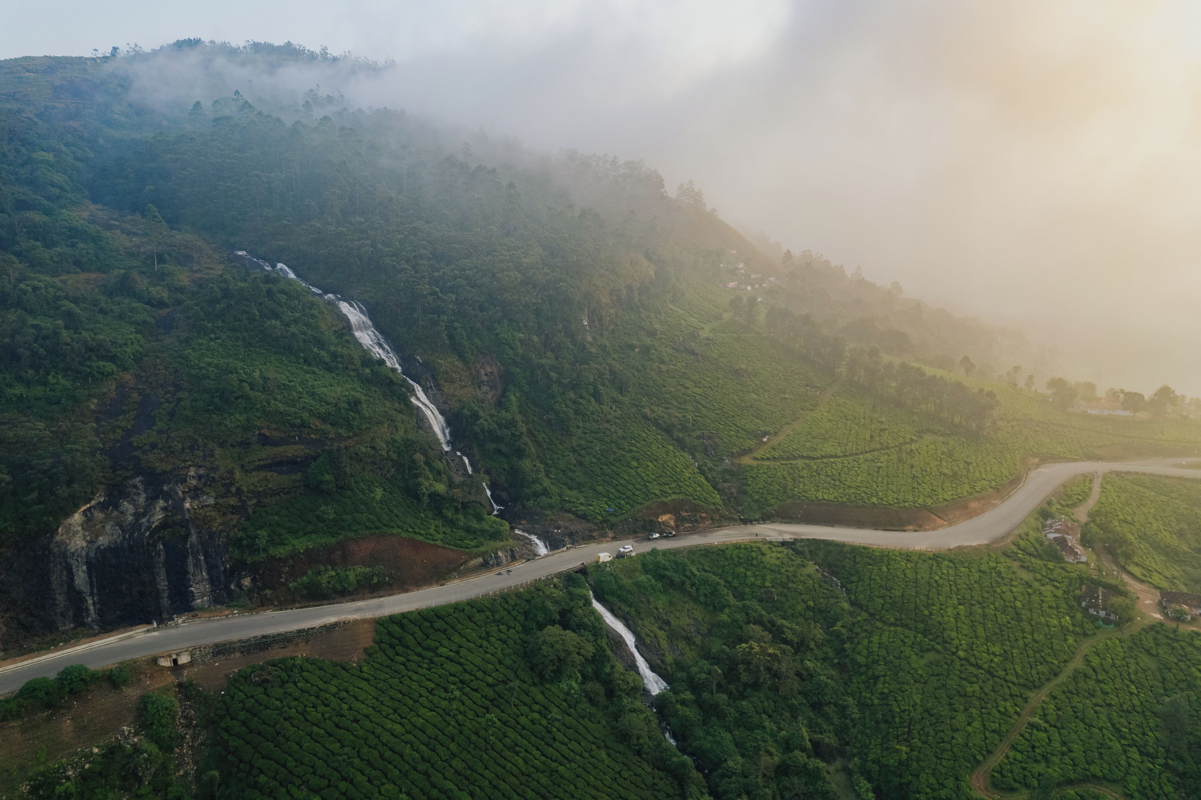 A lush green valley with a waterfall, terraced fields, and a winding road.
