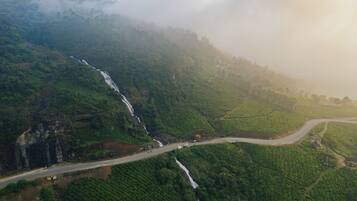A lush green valley with a waterfall, terraced fields, and a winding road.